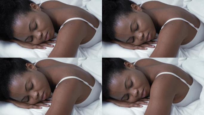 安详的非洲裔美国妇女睡在舒适的床上，躺在柔软的枕头矫形床垫上，平静的年轻黑人女士躺在卧室的白色床单上