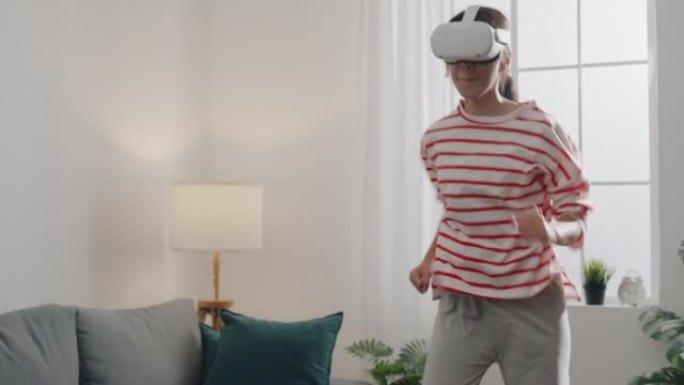 年轻女子戴着VR耳机获得体验模拟数字世界跑步玩动作模拟器游戏手机应用程序在家里的客厅。