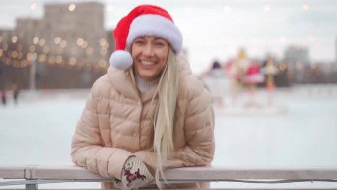 冬天。圣诞节假期，戴着圣诞老人帽子的女人在中央广场的开放城市溜冰场上滑冰。冬季。高加索成年女性业余滑