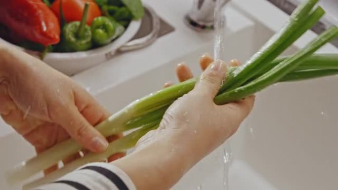 女性手的特写镜头在厨房水槽里洗葱。
