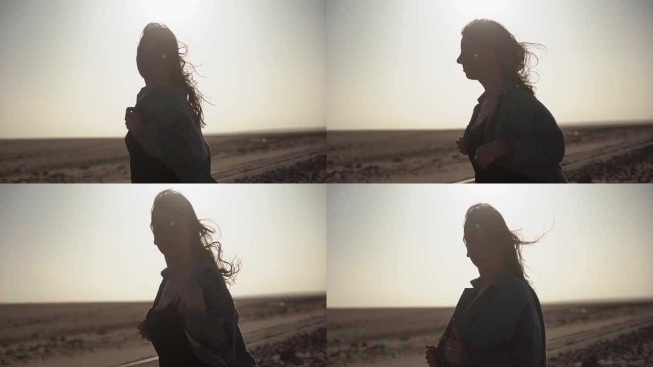 沙漠中年轻女子的剪影。强风中的铁轨上的女孩