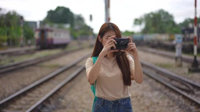 年轻美丽的亚洲女游客用胶卷相机拍照，在火车站平台上微笑和享受，乘坐火车运输度假旅行的快乐旅行生活方式