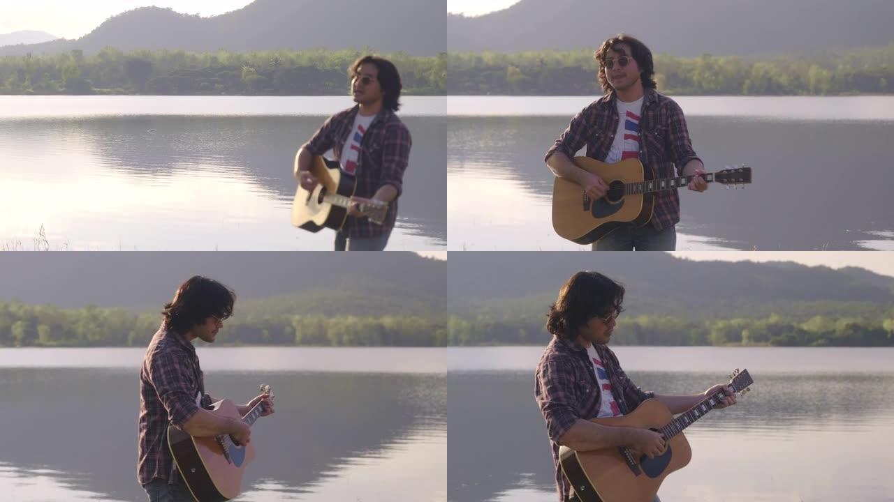 英俊的卷发亚洲男子在日落时在湖边弹吉他和唱歌度假。