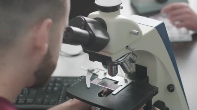 男性微生物学家，医务人员通过显微镜观察血液样本，并在实验室进行分析。实验室助理使用现代显微镜进行生物