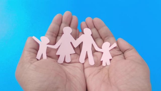 快乐纸家庭在一个男人的手上，手掌朝上，蓝色背景。放大。折纸工艺装饰形状和人物。