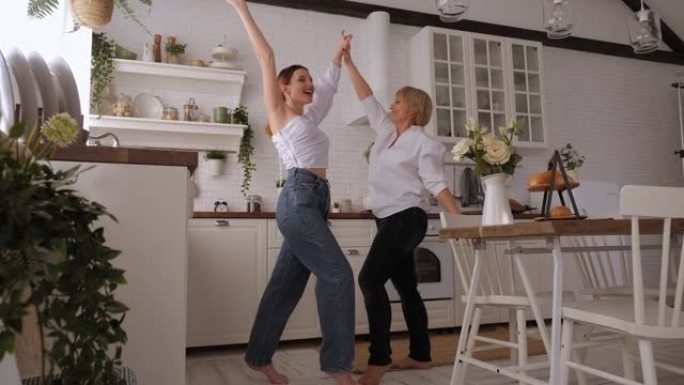 一个开朗的年迈的母亲和一个成年的女儿跳舞，在厨房里玩得开心。