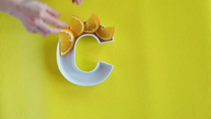 食物概念中的维生素c营养素。女人将橙色切片放在黄色背景上的字母C形状的盘子中。平面或俯视图。抗坏血酸