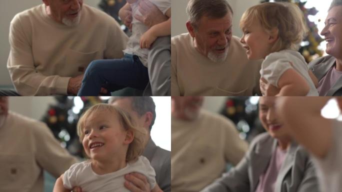 快乐的爷爷奶奶，白发苍苍的爷爷奶奶，一边坐在家里的沙发上，一边拥抱他们心爱的四岁小孙子。家庭假期