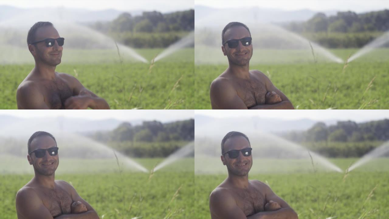 没有穿衬衫的农业工人在有灌溉系统的绿地上工作。背景是洒水器
