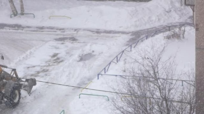 带桶的拖拉机清除了居民楼院子里的积雪。冬天降雪，推土机清理道路。公用事业和运输。强降水雪