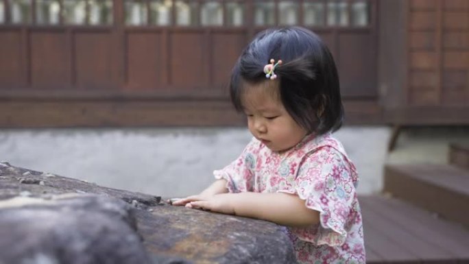 一个无辜的日本蹒跚学步的孩子站在和服的一块大石头附近的特写镜头，正享受着独自在她传统房子附近玩砾石的
