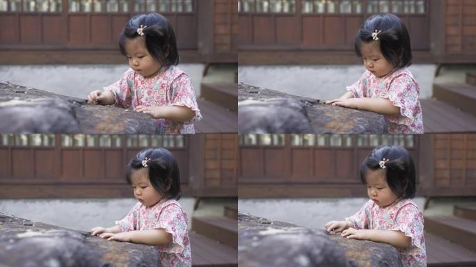 一个无辜的日本蹒跚学步的孩子站在和服的一块大石头附近的特写镜头，正享受着独自在她传统房子附近玩砾石的