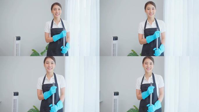 在客厅工作的亚洲清洁服务女工肖像。漂亮的女孩家庭主妇管家清洁工感到快乐，擦窗户做家务或家务，然后看相