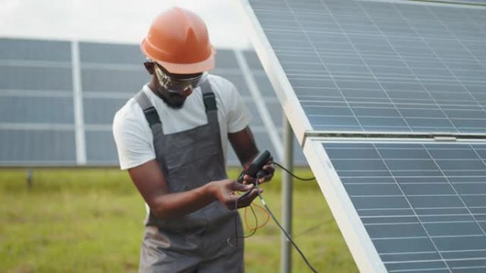 技术员统一使用万用表，同时检查太阳能电池板的电压。非裔美国人控制电站绿色能源的生产。穿着工作服的人测