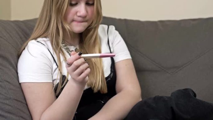 担心的少女坐在沙发上，拿着怀孕测试的肖像。
