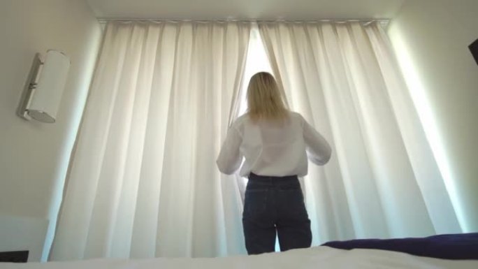 一个穿着白衬衫的女人下床，打开窗户上的窗帘。