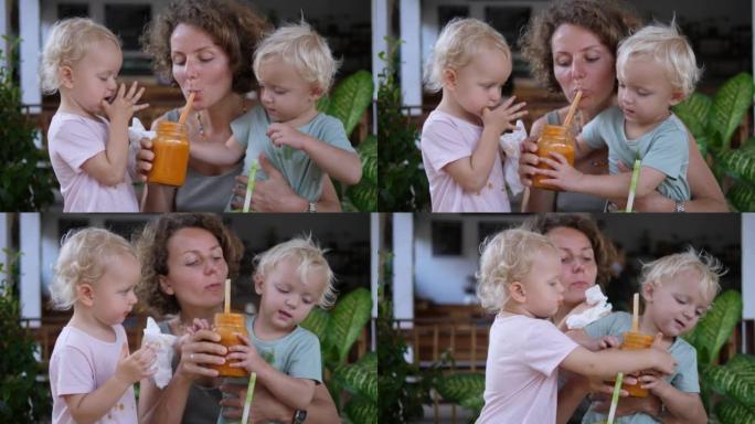 快乐的单身母亲在热带咖啡馆喂养她的双胞胎女儿，凌乱的孩子喝水果冰沙。母亲对她全心全意爱的孩子的关心