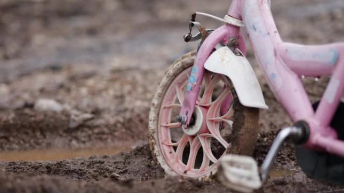泥泞的道路上被遗弃的粉红色儿童自行车，孤独的儿童自行车代表孤独的孩子，无家可归的孩子，孤独的自行车，