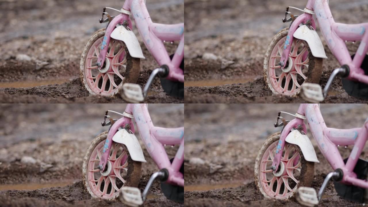 泥泞的道路上被遗弃的粉红色儿童自行车，孤独的儿童自行车代表孤独的孩子，无家可归的孩子，孤独的自行车，