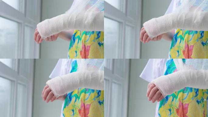 一个孩子手臂骨折的特写镜头。女孩握着折叠在多色t恤背景下的手。手上有石膏的孩子