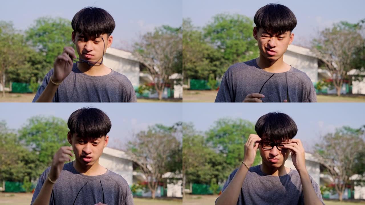 疲惫的年轻亚洲男子眼痛，从眼镜和摩擦他的眼睛在公园。