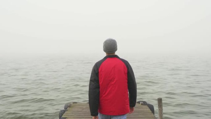 冒险和未知的概念。年轻的男性在木制码头上带着雾走向大海