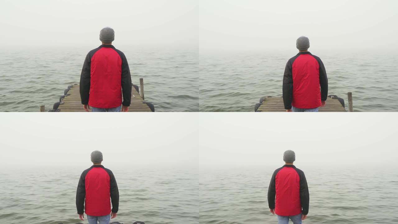 冒险和未知的概念。年轻的男性在木制码头上带着雾走向大海