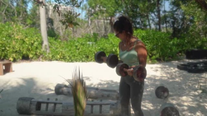 年轻的西班牙裔妇女在海滩上的生态健身房举重