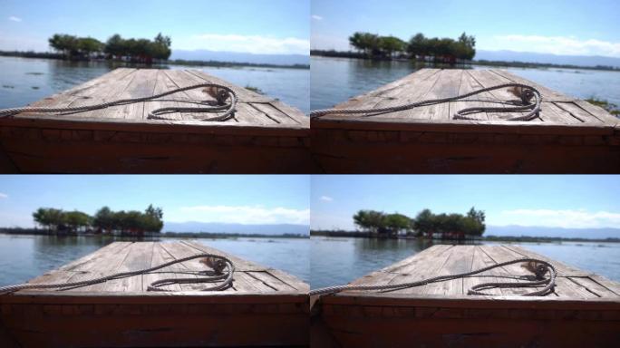 从木船正面看，沿着一个大湖行驶，背景是山和多云的天空。