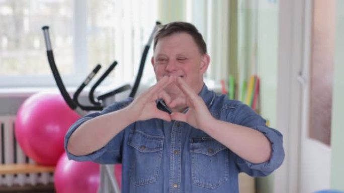 一位患有唐氏综合症的快乐残疾人对着镜头微笑，用手做成心形。