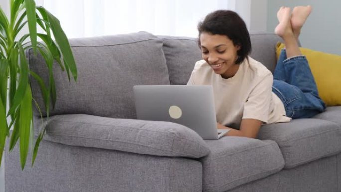 自信的非洲裔美国女孩在智能手机上使用笔记本电脑，坐在家里的沙发上，复制空间