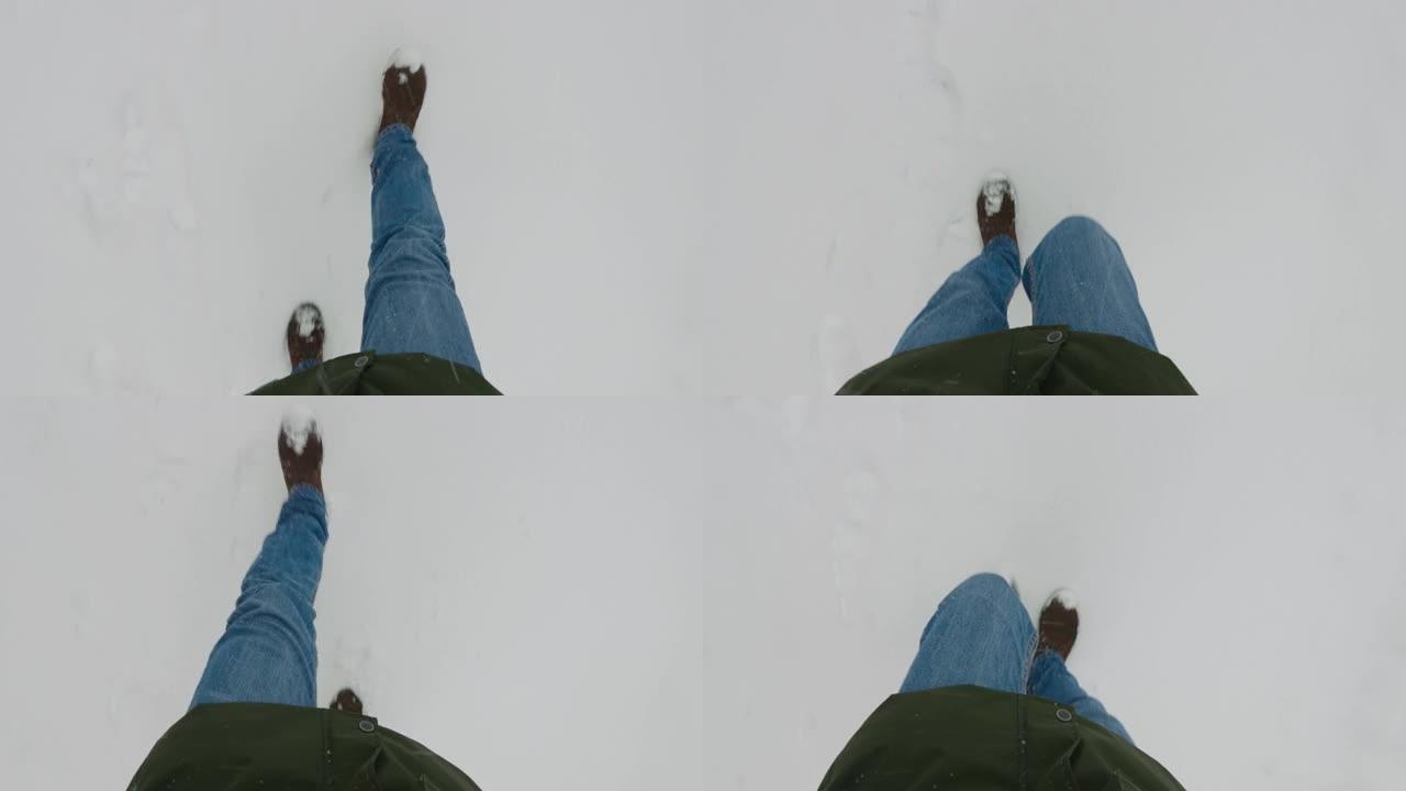 男性腿的俯视图。一名男子穿着时髦的靴子走在积雪覆盖的人行道上