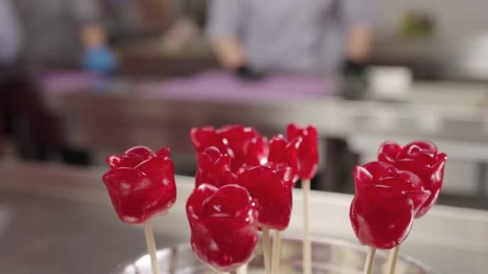 红玫瑰花形式的棒棒糖在糖果店的背景下特写。糖制成的糖果，带有果味。儿童生日聚会上的甜点。慢动作就绪，