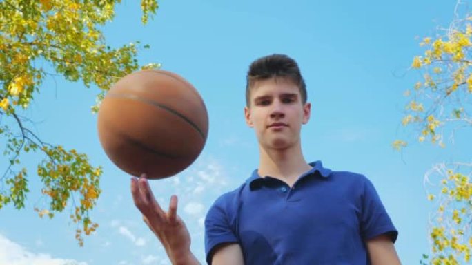 一个年轻的十几岁的男人在篮球场上时用手指旋转球。