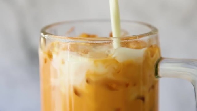 亚洲饮料的冰泰手茶，将新鲜的牛奶倒入玻璃杯中。特写