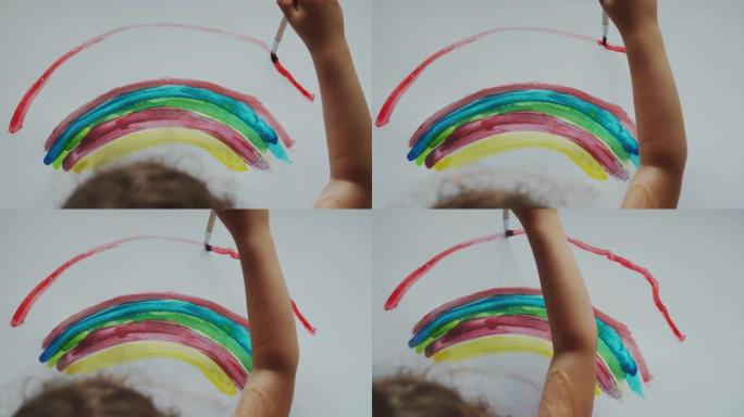 小女孩手里拿着刷子，用彩色颜料在白纸上画彩虹。顶视图镜头