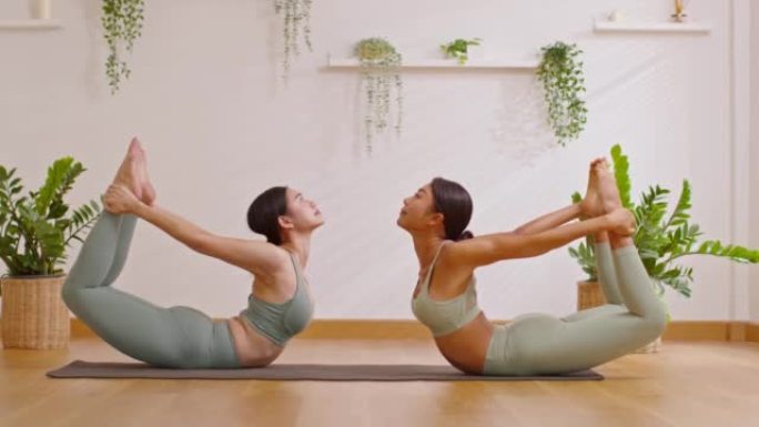 健康夫妇亚洲年轻女子坐在瑜伽垫上做呼吸运动瑜伽弓姿势或dhanurasana姿势一起伸展。两个健康女