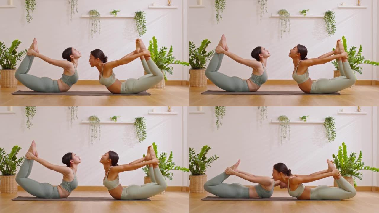 健康夫妇亚洲年轻女子坐在瑜伽垫上做呼吸运动瑜伽弓姿势或dhanurasana姿势一起伸展。两个健康女