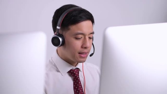 微笑而友好的亚洲呼叫中心接线员戴着带麦克风的耳机，坐在办公室的客户服务部。