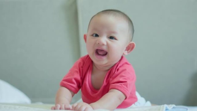 幸福的家庭，可爱的亚洲新生婴儿穿着红色衬衫躺在白色床上玩耍，笑容满面。小天真的新生婴儿可爱的孩子在生