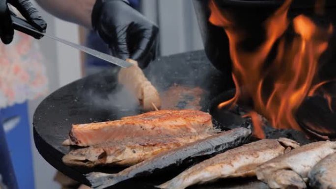 厨师在黑色火盆上烹饪扇贝肉、鲑鱼、臭鱼 -- 特写