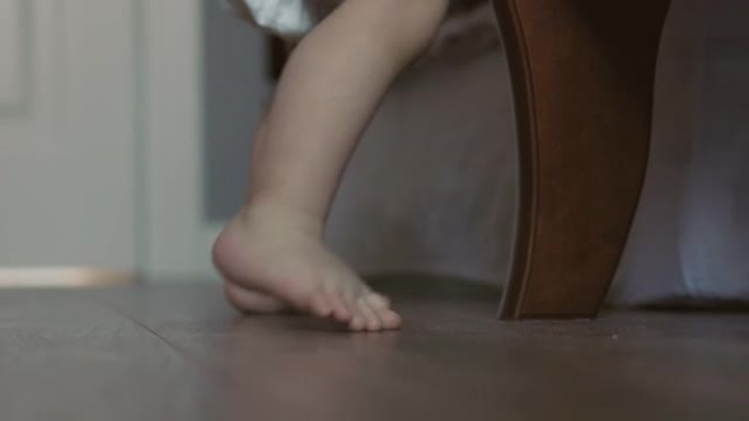 近距离拍摄光脚婴儿在家里踩着木地板。小脚趾踮着脚走