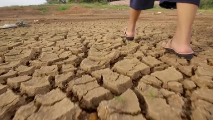 女人在破裂的土壤或破裂的地面上行走当前的干旱问题