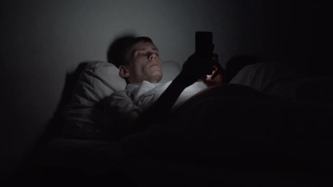 男子晚上躺在床上，使用智能手机