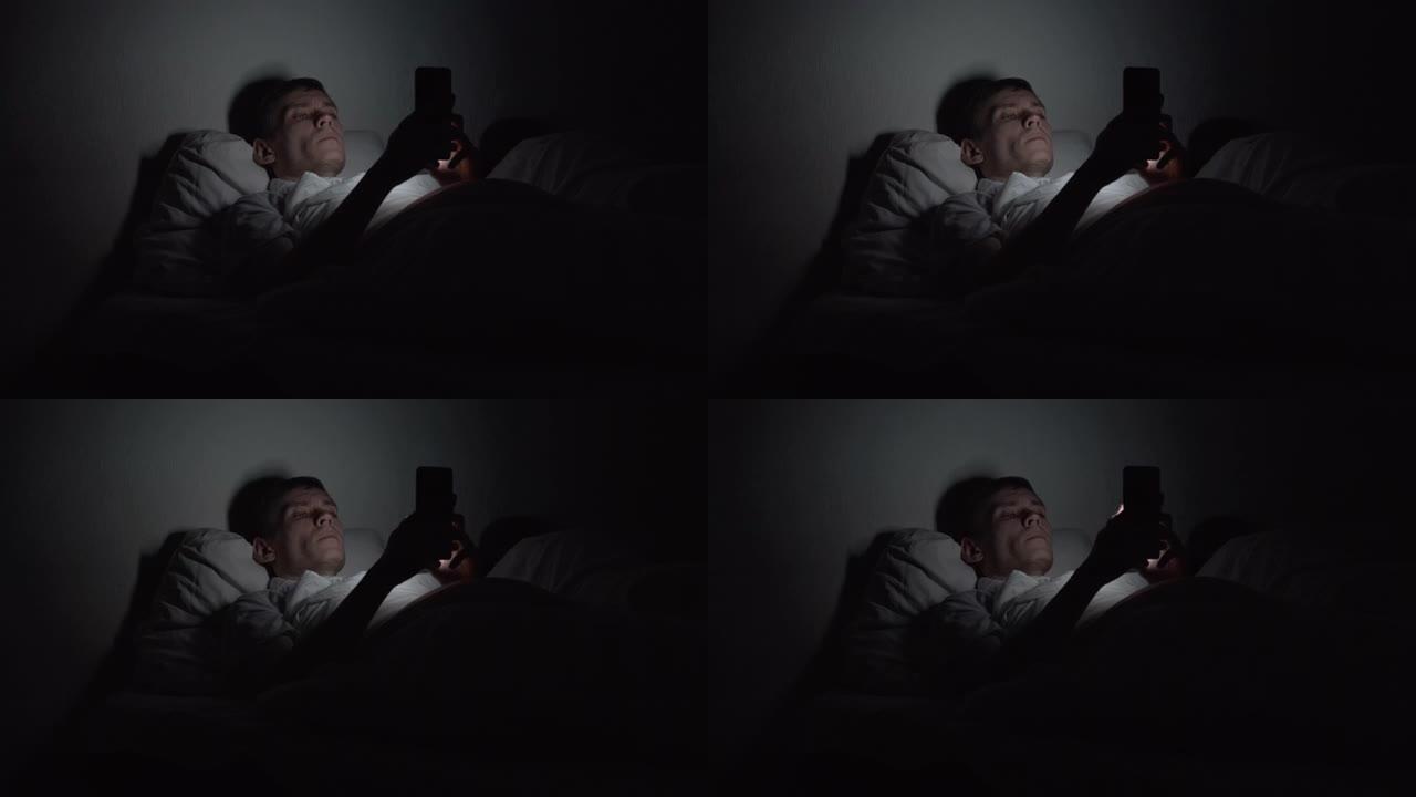 男子晚上躺在床上，使用智能手机