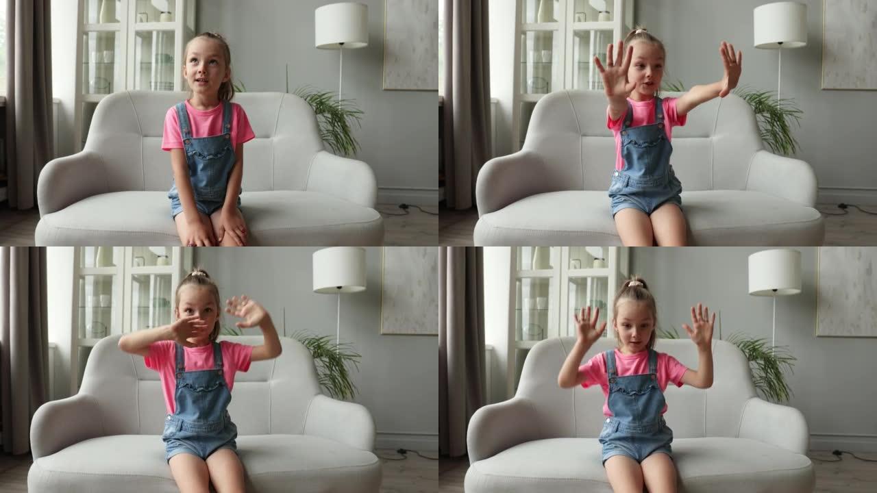 五岁的小女孩，漂亮的脸微笑着看着相机，坐在沙发附近的椅子上，与网络摄像头交谈，进行在线视频通话或录制