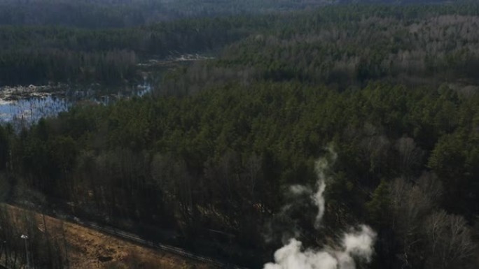 森林和河流附近工厂管道的鸟瞰图烟雾