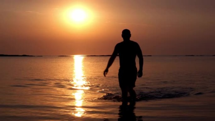 一个肌肉发达的人的轮廓在夕阳的光芒中从海里出来。度假、旅行、自由、健身