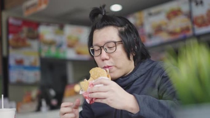 亚洲男子在快餐店吃汉堡和炸薯条。