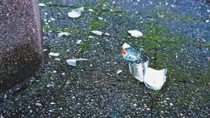 在公共混凝土垃圾箱旁边的人行道上破碎的碎玻璃瓶子碎片